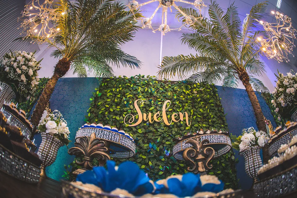 Decoração com palmeiras, painel de folhagens, lustres e nome em letras douradas