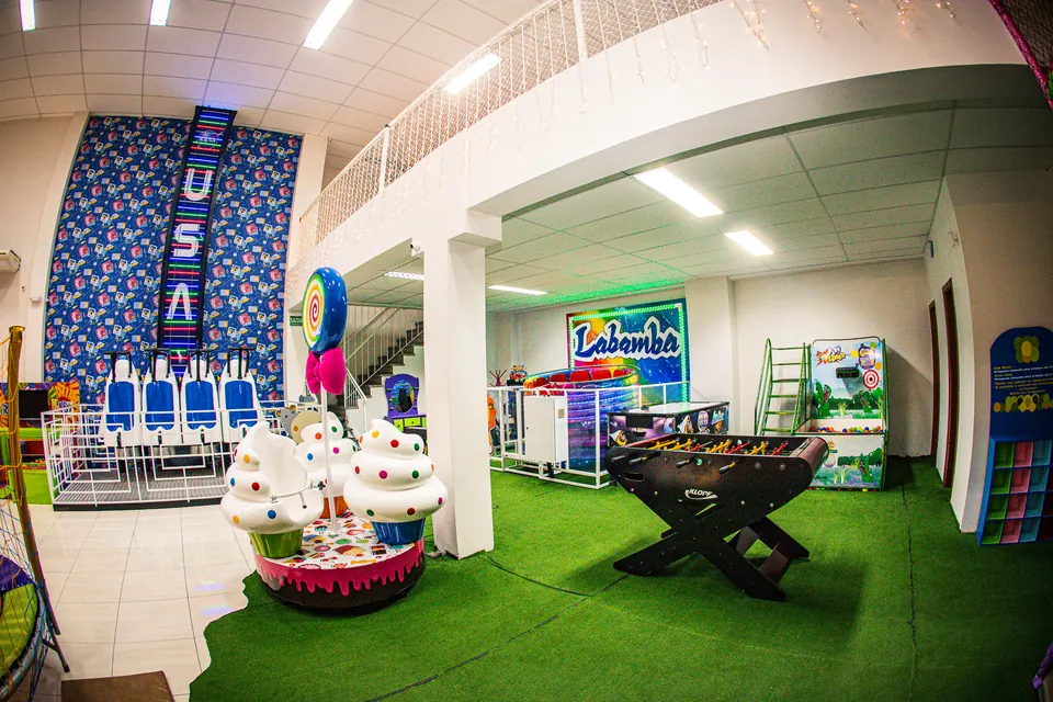 Salão com carrossel de cupcake, pebolim e brinquedos sobre grama sintética