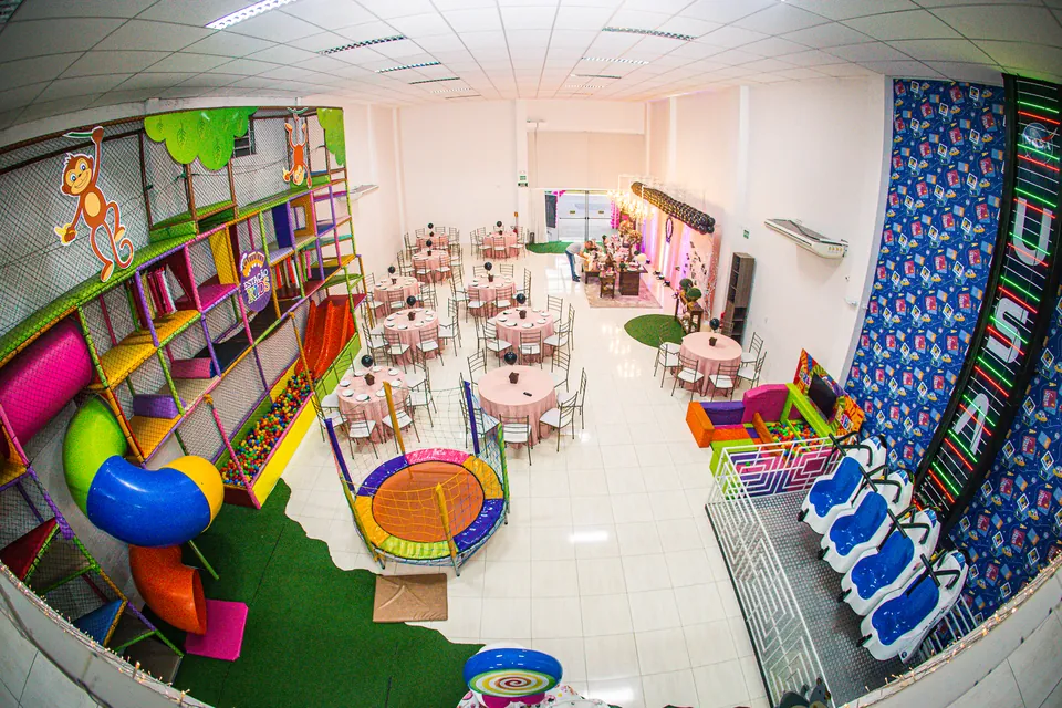 Vista panorâmica do salão principal da Estação Kids com mesas montadas, kid play e brinquedos