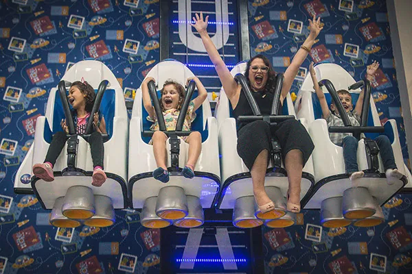 Crianças e adulta vibrando juntas em brinquedo com assentos lado a lado